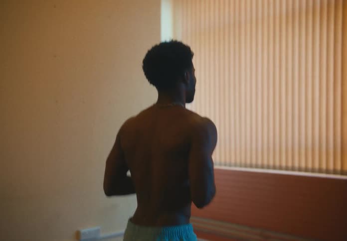 A muscular man jogs in place while standing indoors near a window