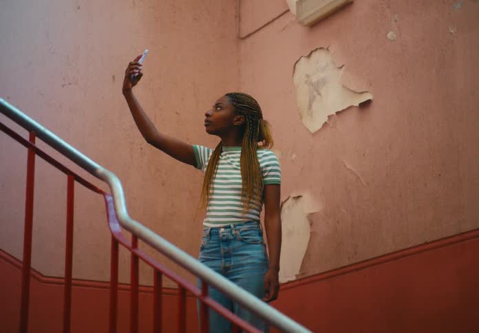 A woman standing in a staircase with a banister and holding up a smart phone and spinning with a wall in the background