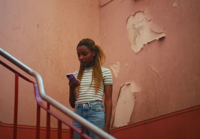 Woman takes selfie on staircase landing next to torn wallpaper before walking down stairs