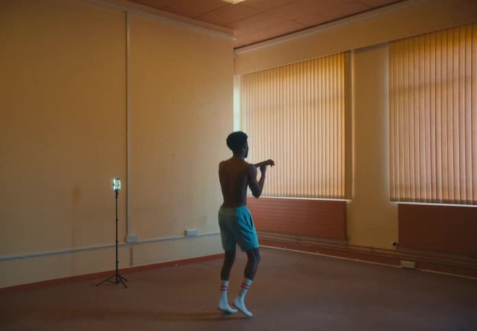 A man in a room shadow boxing with a smartphone on a tripod a wall and windows in the background