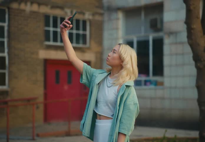 A woman is taking selfies with a cellphone and standing outdoors