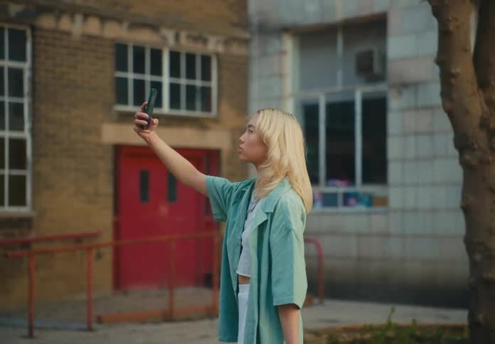 A young woman holds up her smart phone to capture images of herself while she turns around
