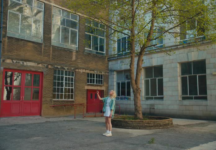 A young asian woman with blonde hair pauses near a building to take a selfie