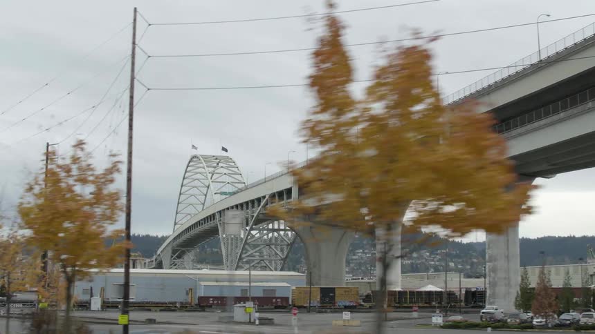 A bridge over a river has rail lines and industrial buildings under it