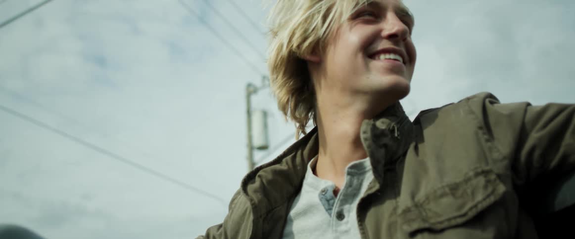 Blonde man wearing jackets sits in vehicle under cloudy sky