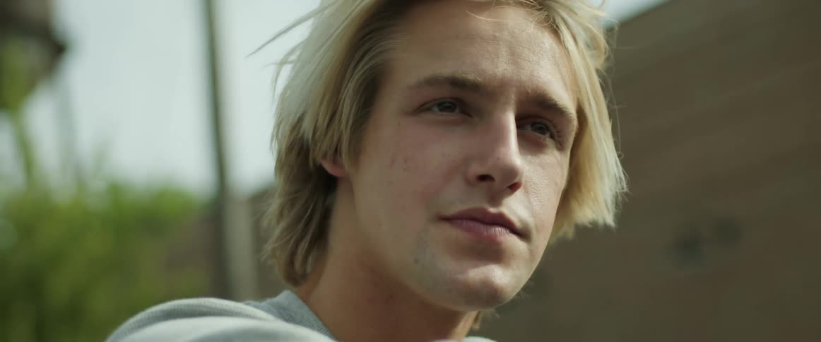 Blonde man rides in open air past building and water tower