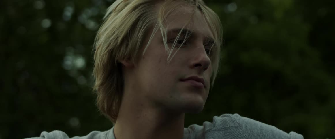 A young male with blonde hair relaxes as he rides in the back of a pickup truck