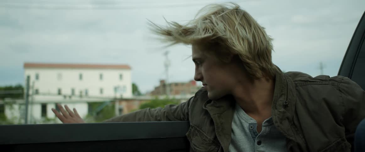 A man riding in the back of a vehicle with trees buildings the sky and clouds in the background