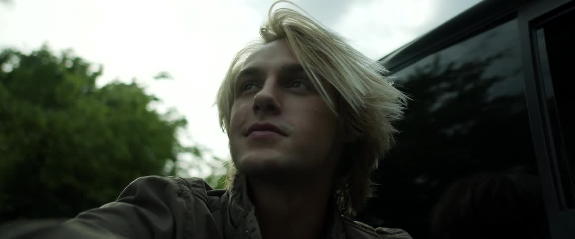 A man riding in the back of a vehicle with trees the sky and clouds in the background
