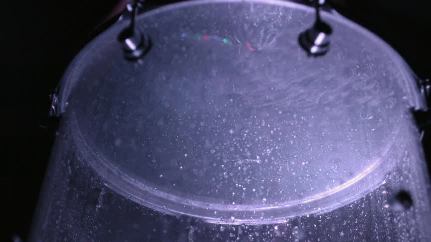 Bubbles go up and down inside a drum that a drummer hits with a stick