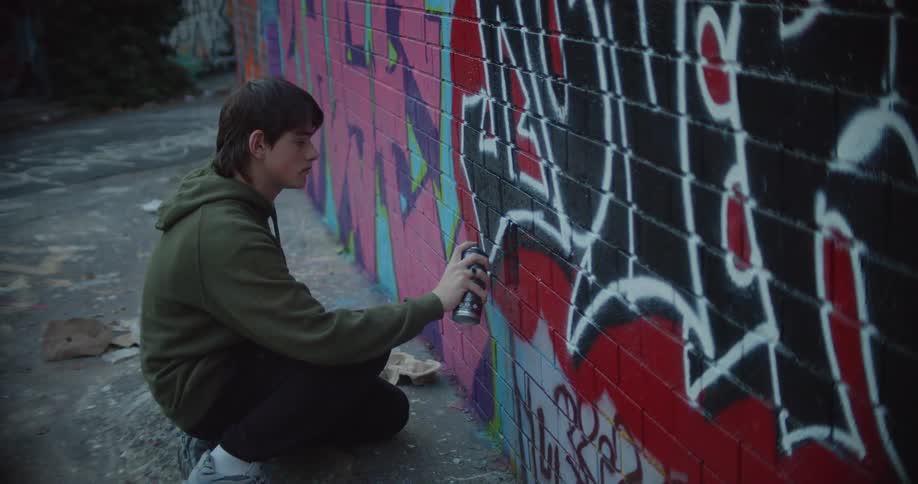 A teenager spray paints on a brick wall already covered with graffiti