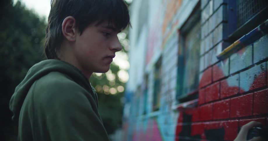 A young man applies spray paint to an art piece on the exterior wall of a building