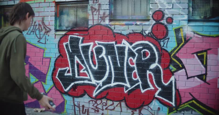 Graffiti artist wearing hoodie adds finishing touches to graffiti art on brick wall