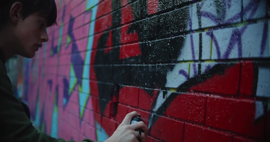 A young man carefully applies spray paint to as he paints a brick wall