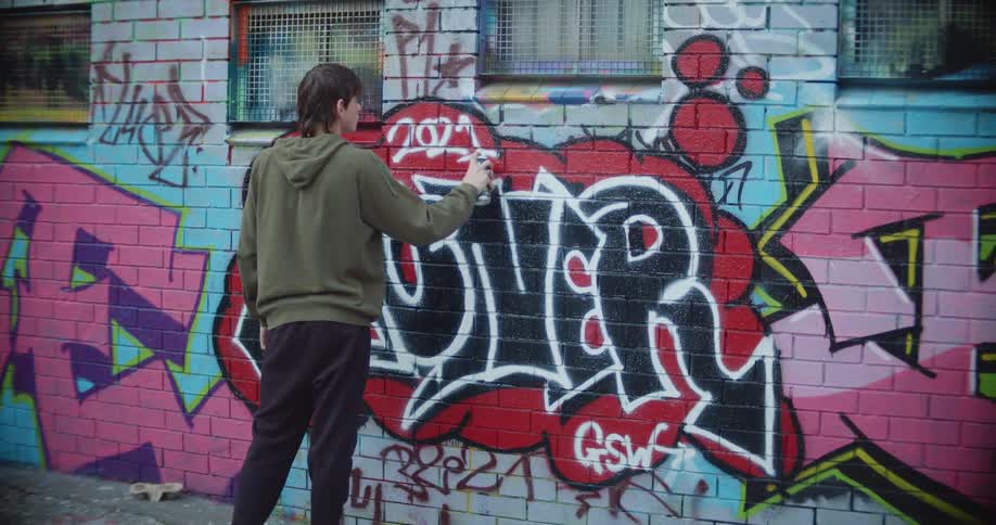 A teenage boy spray paints on a building