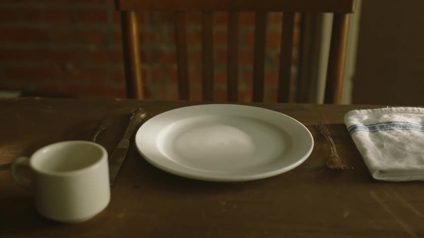 A room with a table and chair with a cup a plate and utensils on the table
