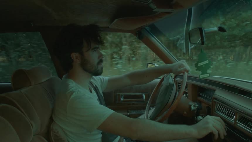 A man driving a vehicle with a steering wheel with trees the sky and clouds in the background