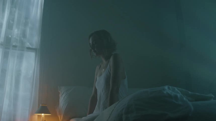 A woman is sitting on a bed indoors at night