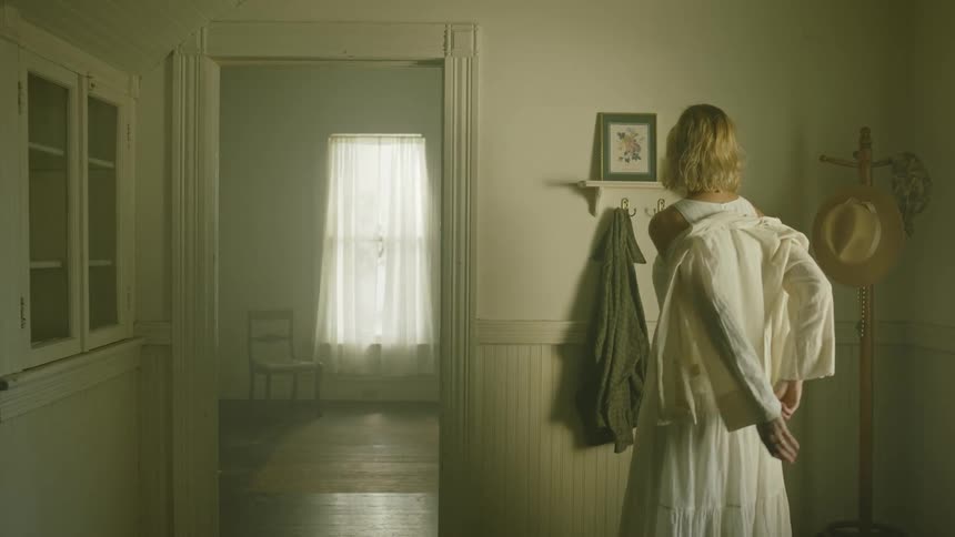 A woman is standing indoors and taking off a jacket