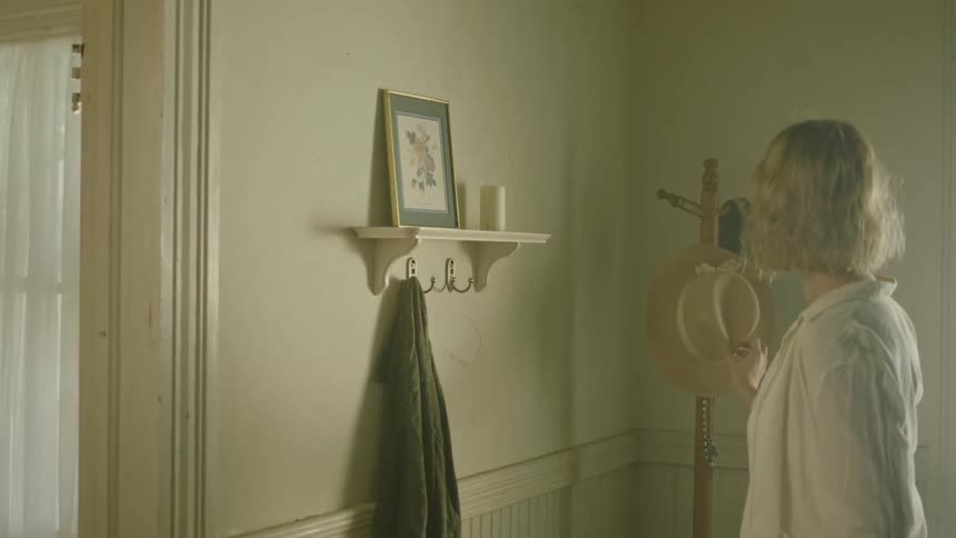 A woman hangs up her hat on a coat rack and takes off her jacket