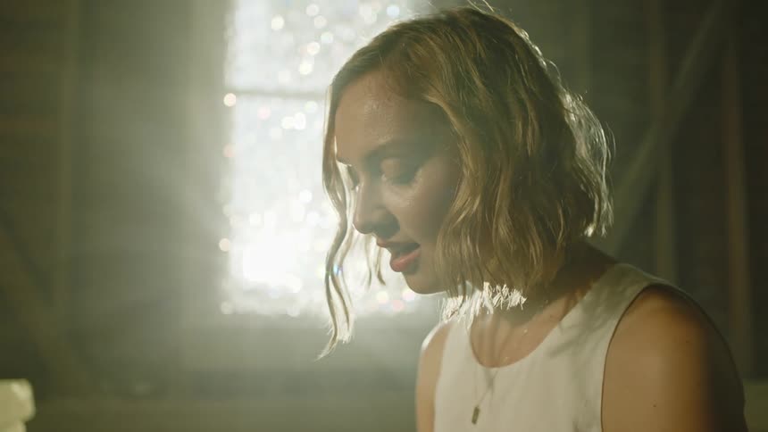 A woman in a room sitting with a wall and window in the background