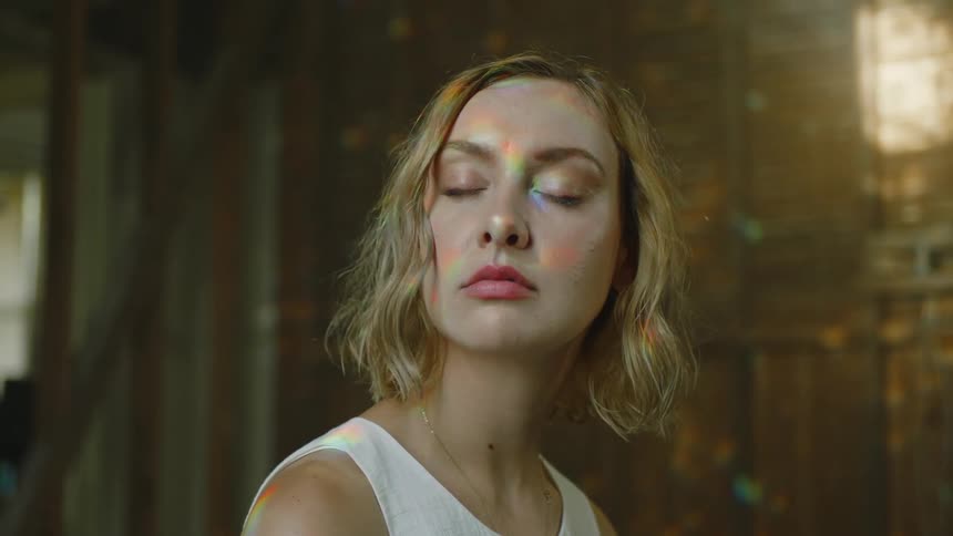 Young blonde woman sitting in a cabin with colorful rainbow lights shining on her face