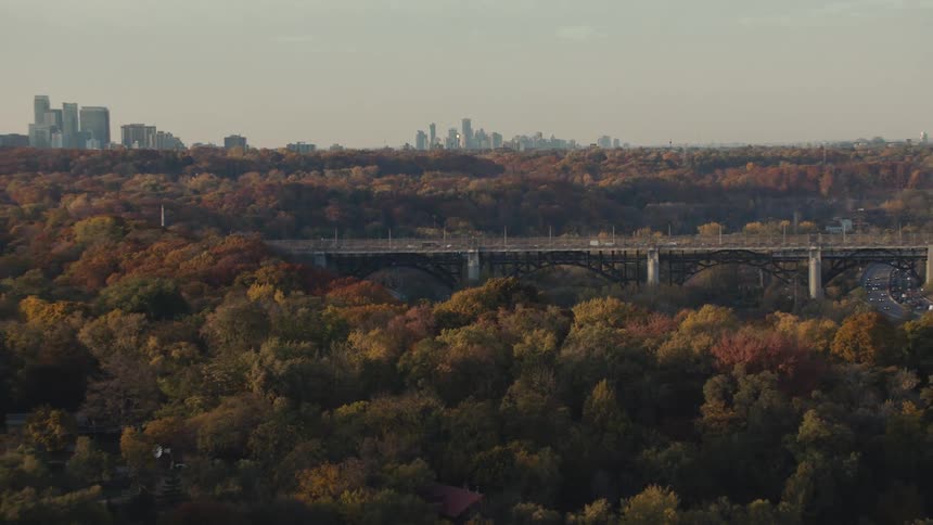 Heavy traffic drives along a bridge surrounded by lush trees with downtown in the distance