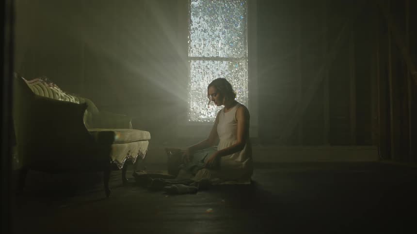 Young woman wearing a white gown sitting on the floor of a dimly lit room
