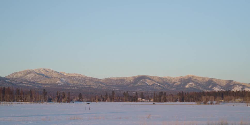 A mountain looms over a snowy grassland under a clear blue sky