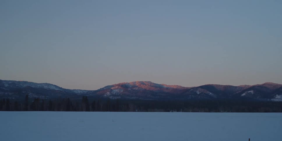 The sun sets over a snow topped mountain and vast field