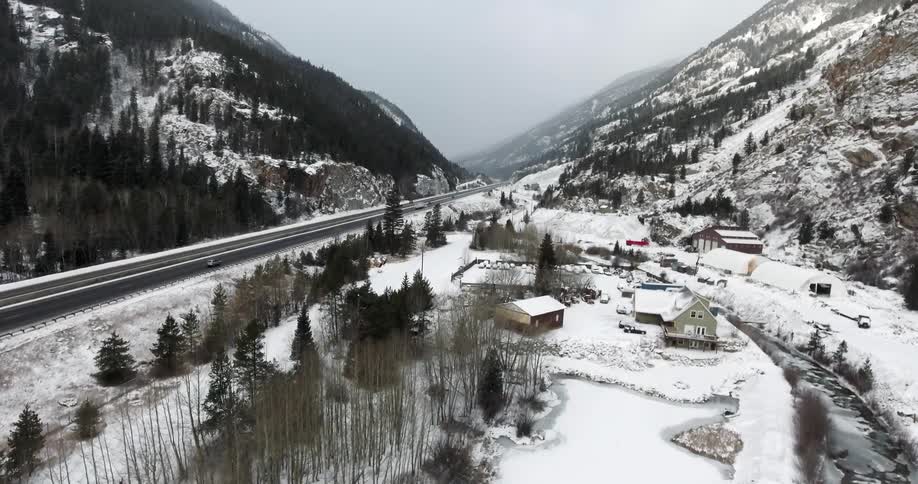 Drone footage of cars travelling along a wintry mountain highway while it snows