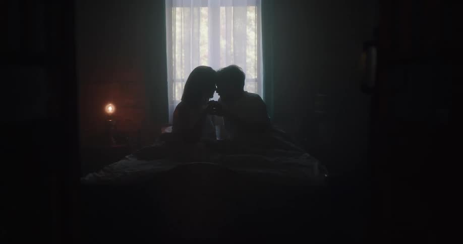 Couple reclining in dark bedroom silhouetted by window touch foreheads