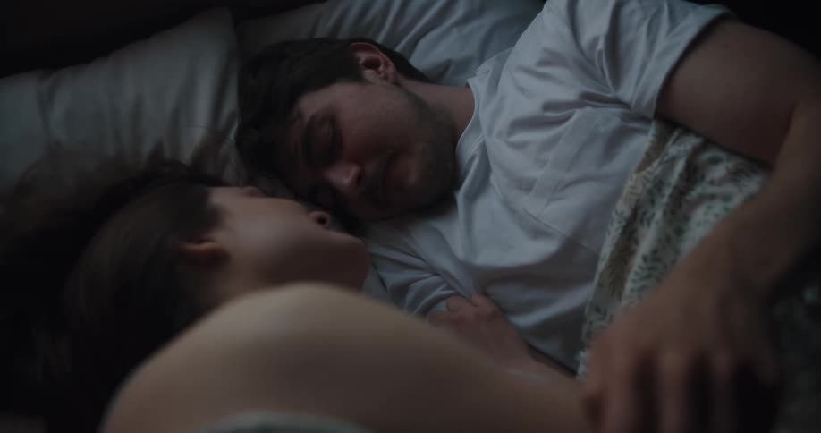 Couple lie in bed together smiling at each other as man strokes womans shoulder