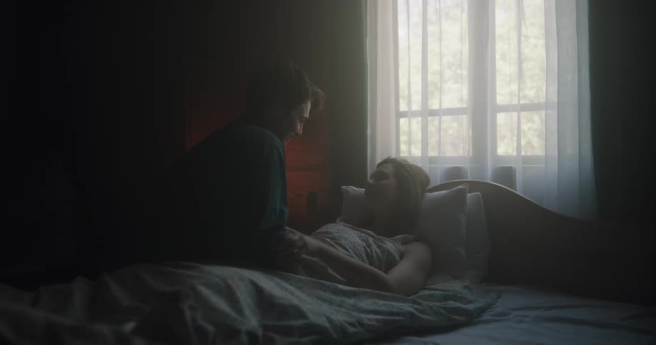 A man checks on his girlfriend in bed and kisses her forehead