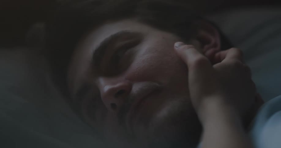 Woman caressing the face of a man laying in bed in the morning