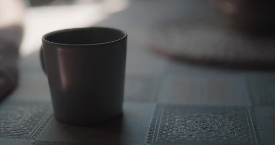 A man picks up a brown ceramic coffee mug from his kitchen table