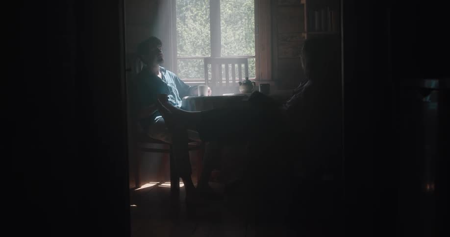 A man and a woman sitting on chairs at a table with a wall and window in the background