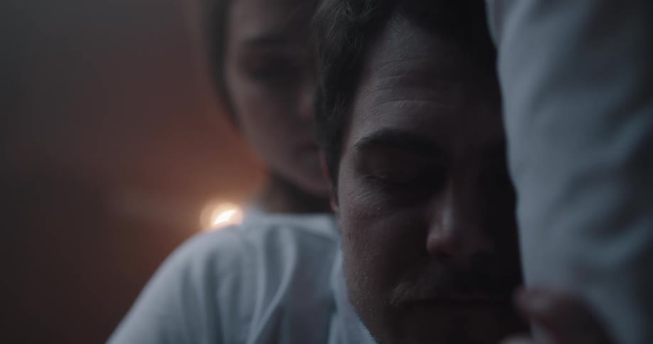 A man and a woman in a bedroom laying on a bed with a wall in the background