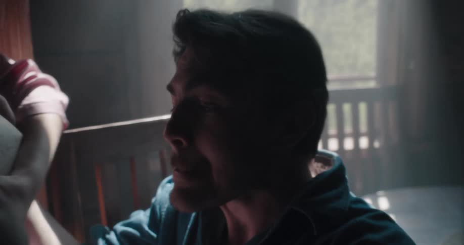 A man and a woman in a room with the woman taking a book away from the man with a wall and window in the background