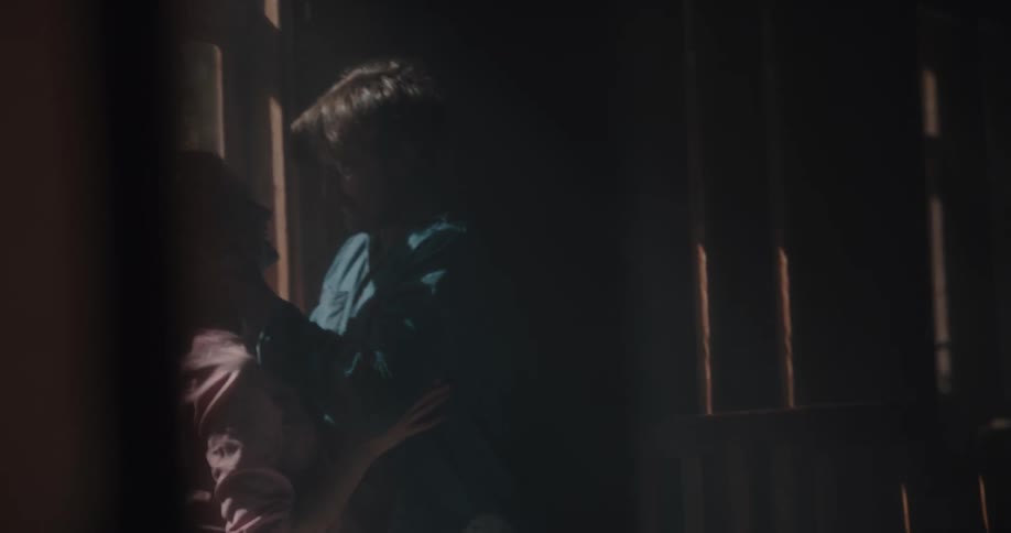 A man and a woman in a room kissing with a wall and window in the background