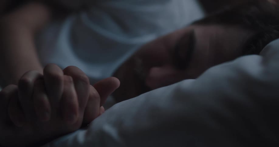 A man and woman lay close to each other in bed as the woman leans near her partner
