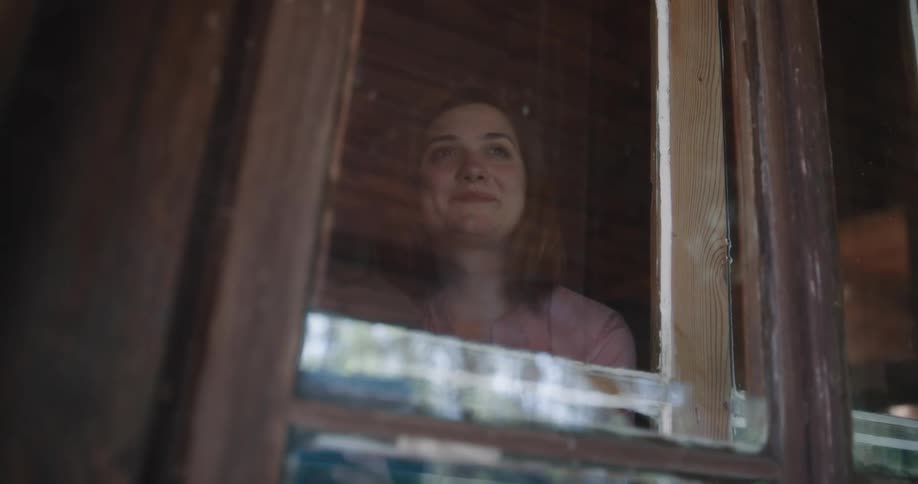 A woman in a room drinking from a mug looking out of a window