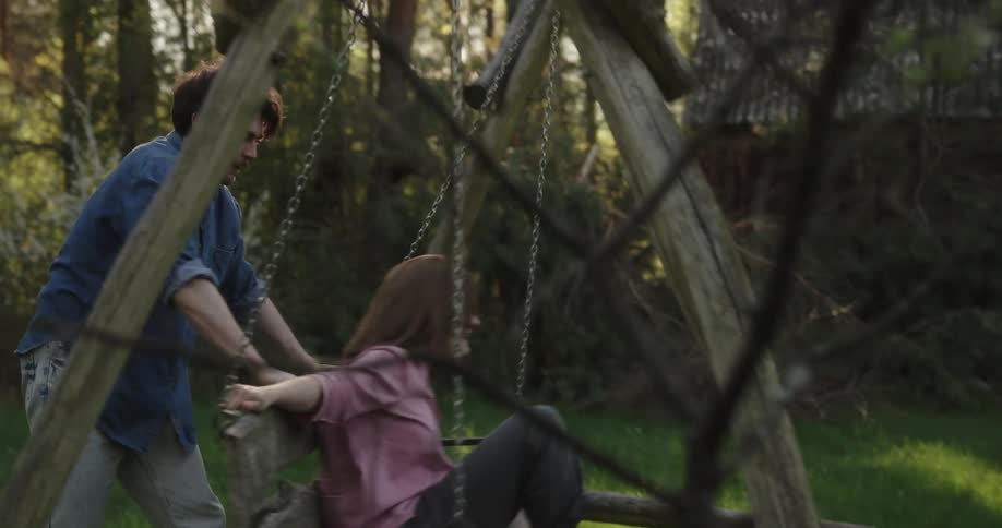 Young couple playing on a wooden swing in near a cabin in the countryside at morning