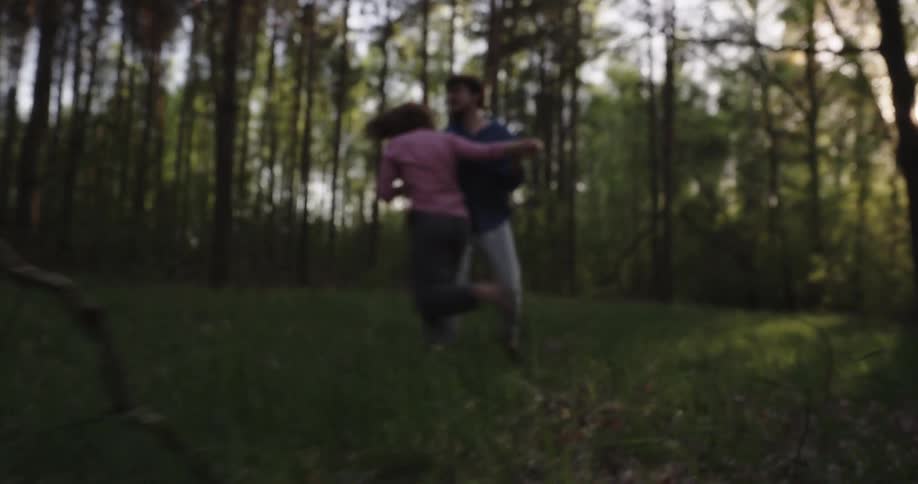 A couple playfully chases each other through a forested area before embracing