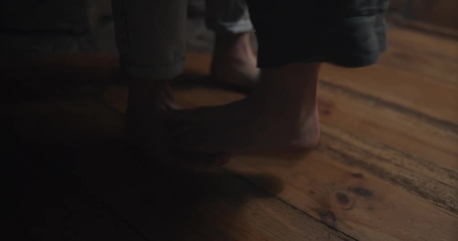 Young couple dancing barefoot over a wooden floor in a dimly lit room