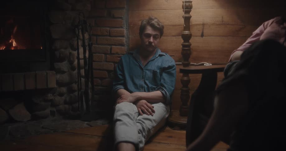 A male and female are sitting indoors by a fireplace