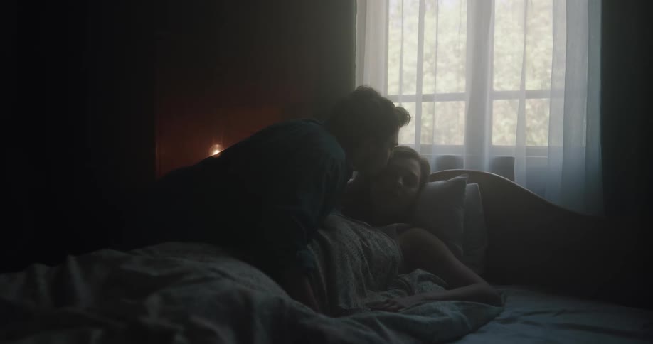 A man wakes a woman by kissing her forehead