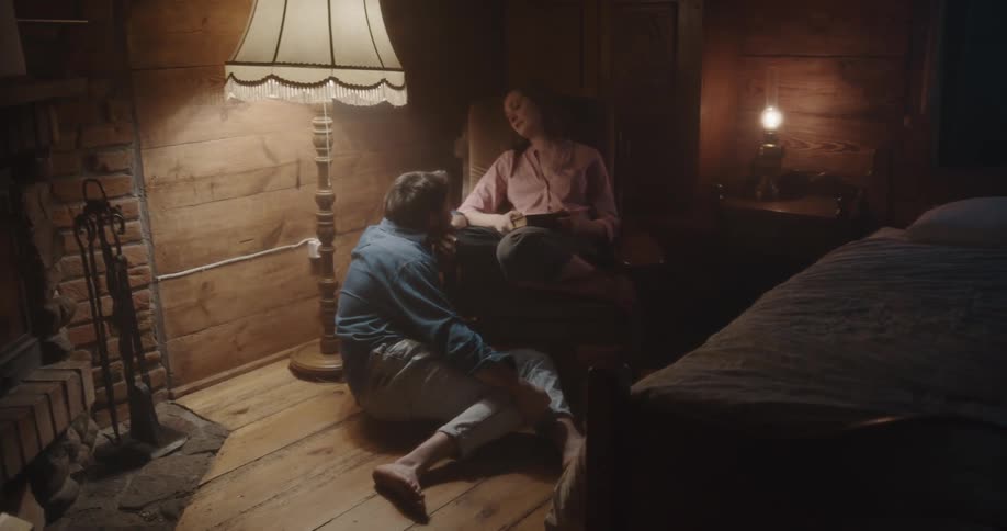 A man scoots on the floor to be closer to his wife in a chair as they relax by a fire in their cabin