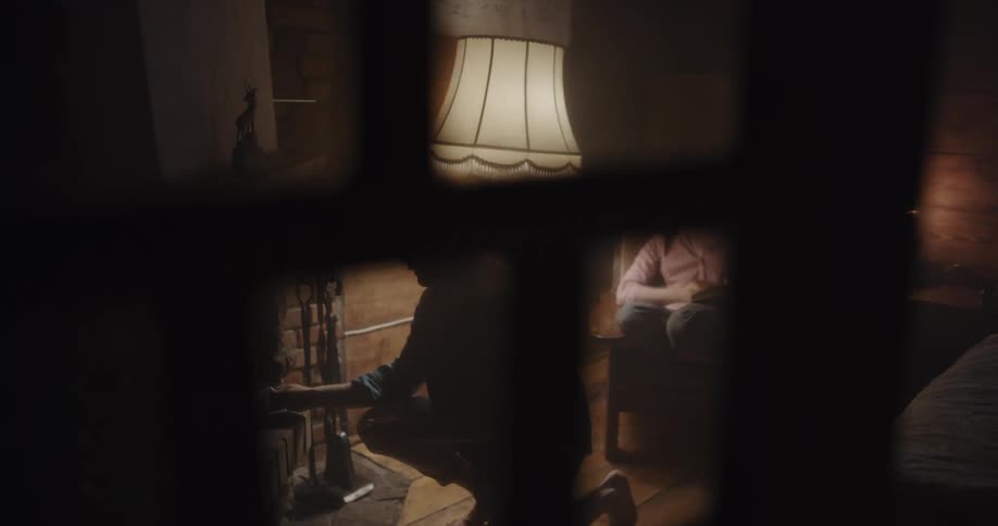 Woman sits in chair as man adds wood to fireplace