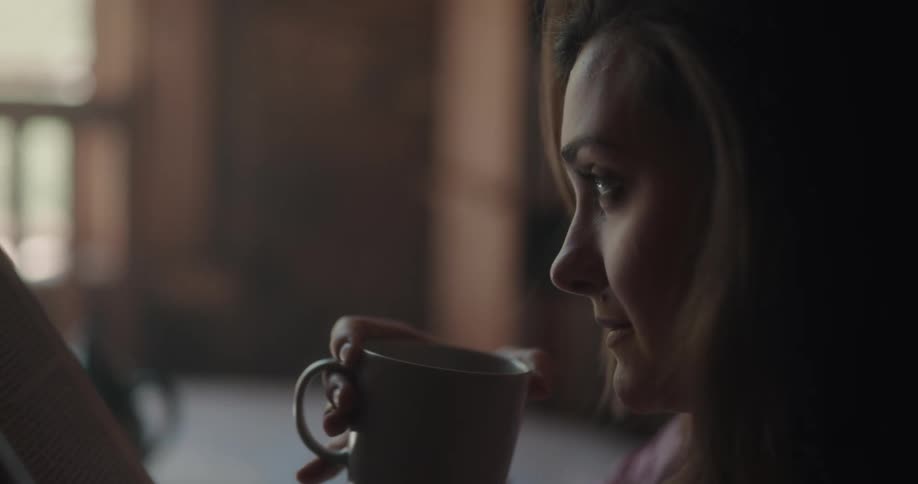 A woman drinking tea from a mug and reading a book